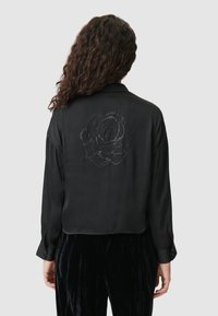 Czarna satynowa bluzka z kołnierzykiem, z różanym wzorem wyłożonym koralikami na plecach. Długie rękawy i mankiety na guziki.