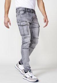 Grijze denim cargobroek met meerdere pockets, gestructureerde naden en een slim fit. Gecombineerd met wit en grijs sportschoenen.
