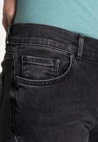 Černé džíny z denimu mají klasický střih, zadní kapsu a detaily švů. Materiál má jemnou texturu a pás je viditelný.