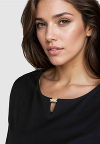 Black top featuring a keyhole neckline adorned with a small metallic accent. Smooth fabric with a relaxed fit and subtle texture.