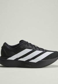 Scarpa da corsa nera con design a tre strisce bianche, lacci neri, suola spessa etichettata Lightstrike Pro, posizionata su uno sfondo chiaro semplice.