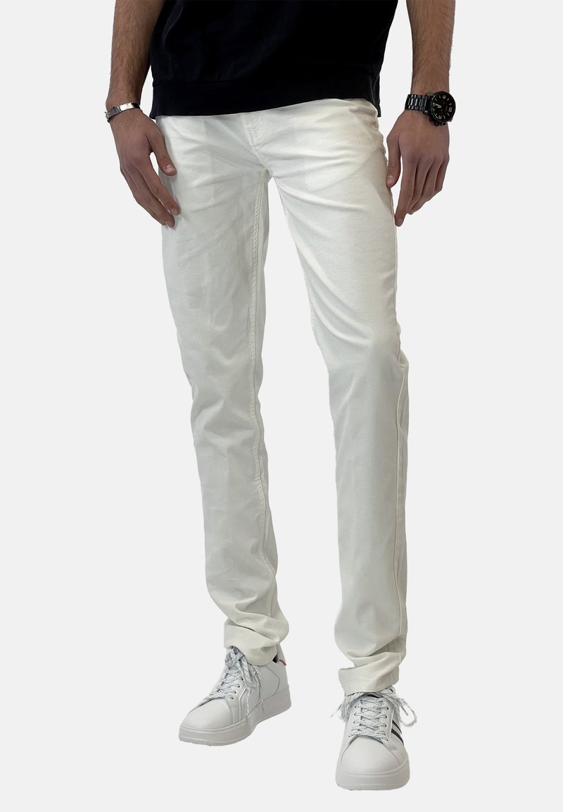 Pantalones de algodón ajustados y blancos con una textura suave, combinados con zapatillas blancas. El conjunto incluye una blusa negra y accesorios mínimos.