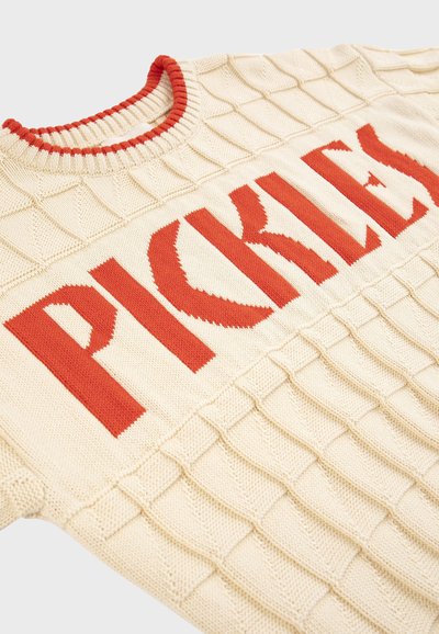Pull en tricot crème avec col côtelé rouge et texte rouge audacieux "PICKLES" sur la poitrine, présentant des motifs géométriques en relief.