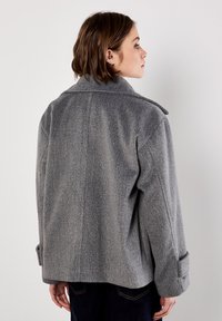 Giacca in misto lana grigia con un ampio colletto, spalle scese e maniche con risvolto; presenta una finitura texturizzata e una vestibilità rilassata.
