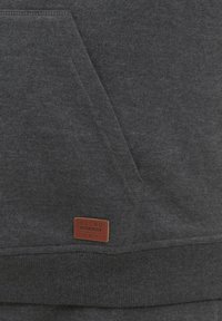 Sudadera gris con un tejido texturizado, bolsillo tipo canguro, dobladillo acanalado y una pequeña etiqueta de cuero marrón con "BLEND" grabada.