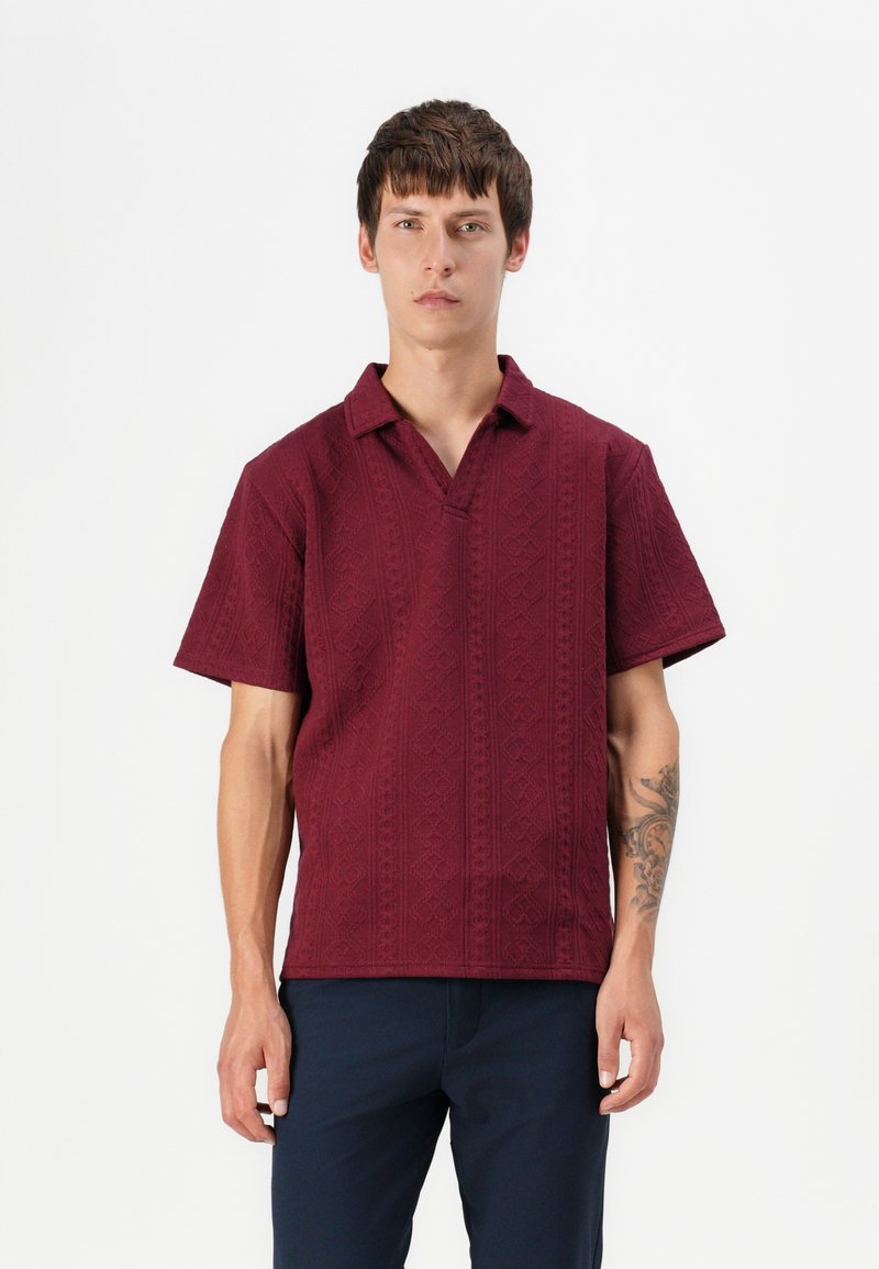 Chemise bourgogne à manches courtes avec un motif texturé et col ouvert. Portée avec un pantalon marine. Présente une coupe décontractée et un design géométrique distinct.