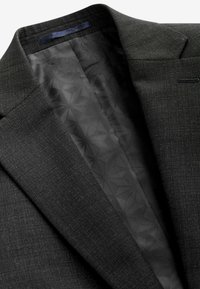 Dunkelgrauer Blazer mit einer strukturierten Stoffaußenseite und einem glatten, gemusterten schwarzen Futter, das geometrische Designs aufweist.