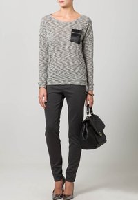 Ljusgrått stickat tröja med svart ficka, matchat med mörkgrå byxor. Modellen håller en svart handväska och bär grå höga klackar. Texturerad tyg.