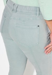 Jeans de mezclilla de un suave color verde azulado. Sus características incluyen una cinturilla elástica alta y un bolsillo trasero con un detalle de remache negro.
