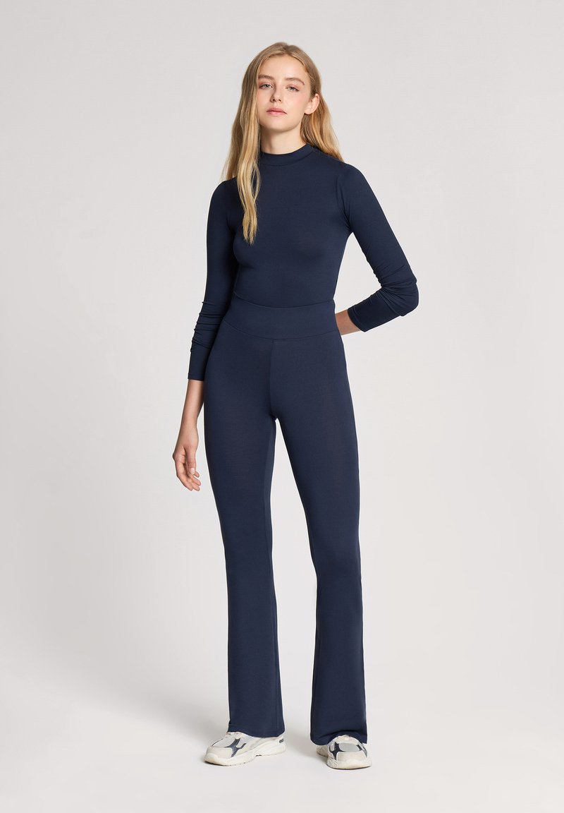 Body blu navy a maniche lunghe abbinato a pantaloni a campana coordinati. Il tessuto sembra liscio, elastico e aderente con una vita alta.