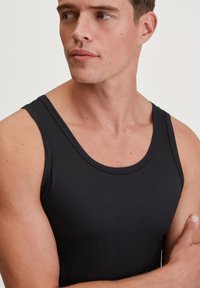 Black tank top made of soft, smooth fabric. Features a rounded neckline and wide shoulder straps, allowing for comfortable movement.