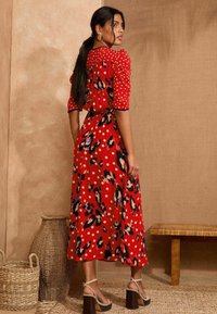 Rdeča obleka s pikami in vzorcem leopardjega krzna. Kratki napihnjeni rokavi, pasni trak in dolg rob. Model nosi sandale z blokastimi petami.