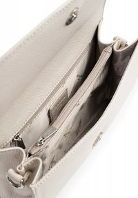 Interno di una borsa a mano in pelle beige con scomparto con zip. Presenta due sezioni e una trama liscia, con dettagli del logo in modo discreto sul tessuto.