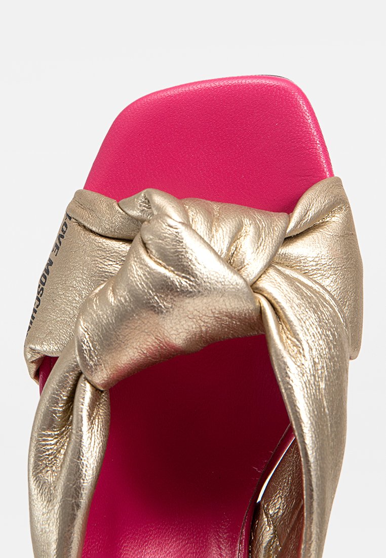 Goldfarbene, metallische Rutsch-Sandale mit gedrehtem Knoten-Detail und einer leuchtend pinken Innensohle. Flache Sohle und keine sichtbaren Beschläge.