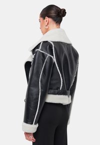 Giacca cropped in pelle nera con colletto e polsini in pelliccia bianca, caratterizzata da cuciture a contrasto e un design strutturato.