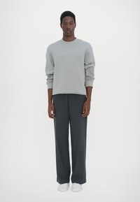 Gray sweatshirt with ribbed cuffs, paired with dark gray wide-leg pants and white sneakers. Simple design with no visible logos.