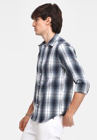 Gevlekt knoopshirt in marineblauw, wit en lichtblauw. Zachte stof met een relaxte pasvorm en opgerolde mouwen. Zijzak zichtbaar.