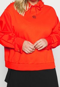 Jasně oranžová mikina s vysokým límcem, stahovací šňůrkou a elastickými manžetami. Na prsou se nachází malé černé logo Nike.