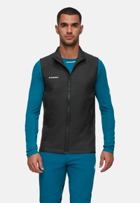 Schwarze isolierte Weste mit hohem Kragen, Frontreißverschluss und Seitentaschen; Modell trägt ein blaues Langarmshirt und eine Hose.