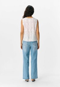 Haut sans manches blanc brodé avec une ouverture en clé à l'arrière, associé à un jean large bleu clair. Tissu lisse et design texturé.