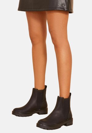Black Chelsea boots made of smooth leather, featuring elastic side panels, a rounded toe, and a chunky rubber sole for stability.