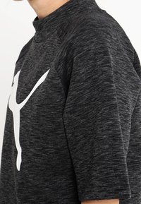 Ciemnoszara, krótka bluzka z krótkim rękawem z wysokim kołnierzem; posiada duże białe logo na przodzie oraz teksturowany materiał.