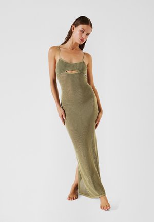 Abito in maglia verde oliva con un design aderente, caratterizzato da spalline sottili e un dettaglio con taglio sotto il busto, lungo fino al pavimento con uno spacco laterale.