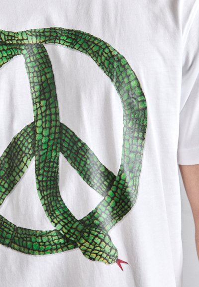 Camiseta blanca con un gráfico de serpiente verde entrelazada formando un símbolo de paz, con detalles de escamas y una lengua roja.
