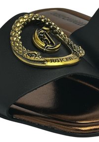 Les sandales noires à glissière présentent une sangle texturée avec un design de serpent en or et un détail de logo. La semelle est lisse et a une finition bronze.