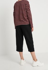 Bordeaux-rot und pink gestreiftes Langarmoberteil, kombiniert mit lockeren, schwarzen, knöchellangen Hosen und weißen, klobigen Sneakers. Matte Stoffqualität mit lässiger Passform.