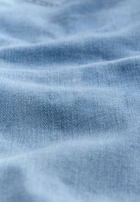 Világoskék farmeranyag lágy tapintással, finom szövésmintával és enyhe fényességgel, amely enyhe gyűrődéseket és redőket mutatva van elrendezve.