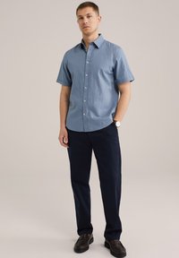 Gaiši zila īsām piedurknēm pogājama krekls ar apkakli, kombinēts ar tumši ziliem biksēm. Gluda auduma struktūra un brīva piegriezuma. Brūni apavi.