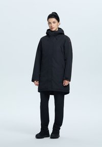 Svart vattentät parkas med huva, långa ärmar och sidofickor. Design i en enhetlig färg med en slät textur och minimalistiska metalldetaljer.