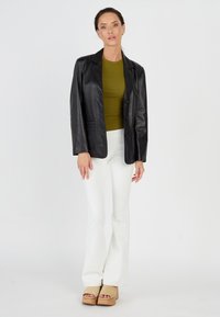 Zwart leren blazer met een losse pasvorm, groene top, witte flared jeans en tan platform sandalen. Gladde textuur en eenvoudig ontwerp.