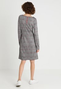 Robe écossaise grise et rouge avec des manches longues, un col rond et un détail de fermeture éclair à l'arrière, fabriquée dans un tissu doux.