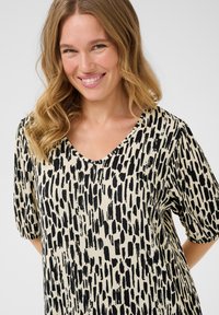 Black and cream patterned top featuring a V-neck, short sleeves, and a textured fabric with a brushstroke design.