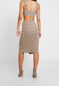 Braun kariertes Zweiteiler-Set mit einem taillierten Crop-Top mit breiten Trägern und einem hoch geschnittenen Midirock. Körperbetonte Silhouette. Schlangenleder-Print-Absätze.