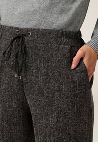 Suéter gris combinado con joggers negros texturizados que cuentan con una cintura con cordones y bolsillos laterales. La tela tiene un patrón moteado.