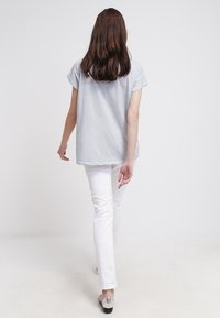 Top gris de manga corta, ajuste relajado, combinado con pantalones blancos ajustados y zapatos plateados. La modelo está de espaldas a la cámara.