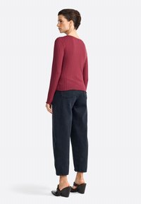 Haut long à manches ribbed bordeaux avec un col rond, associé à un pantalon noir ample et des mules à talons noires. Détails remarquables au dos.