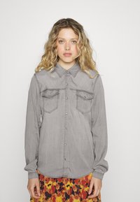 Grijze denim overhemd met lange mouwen en een button-down kraag, twee borstzakken en drukknoopsluiting. Zachte textuur met een subtiele glans.