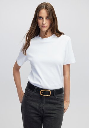 T-shirt bianco in cotone con maniche corte, scollo rotondo, abbinato a jeans neri a vita alta e una cintura nera con fibbia dorata.