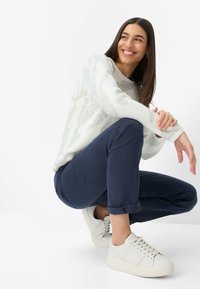 Hvid, struktureret sweater med et subtilt mønster, kombineret med marineblå tapered bukser og hvide sneakers. Outfittet har op-rullede ærmekanter og en afslappet pasform.