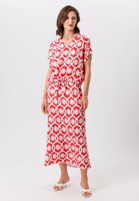 Robe maxi à motifs rouges et blancs avec un col en V et des manches courtes, cintrée à la taille avec une jupe fluide. Texture de tissu lisse.