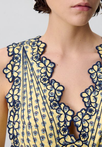 Vestito giallo caratterizzato da ricami floreali con accenti blu navy, scollo a scallop e dettagli plissettati su tutta la stoffa.