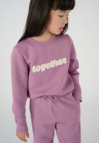 Completo sportivo viola con collo rotondo e vita elastica. "insieme" in ricamo testurizzato color crema. Materiale morbido e vestibilità rilassata.