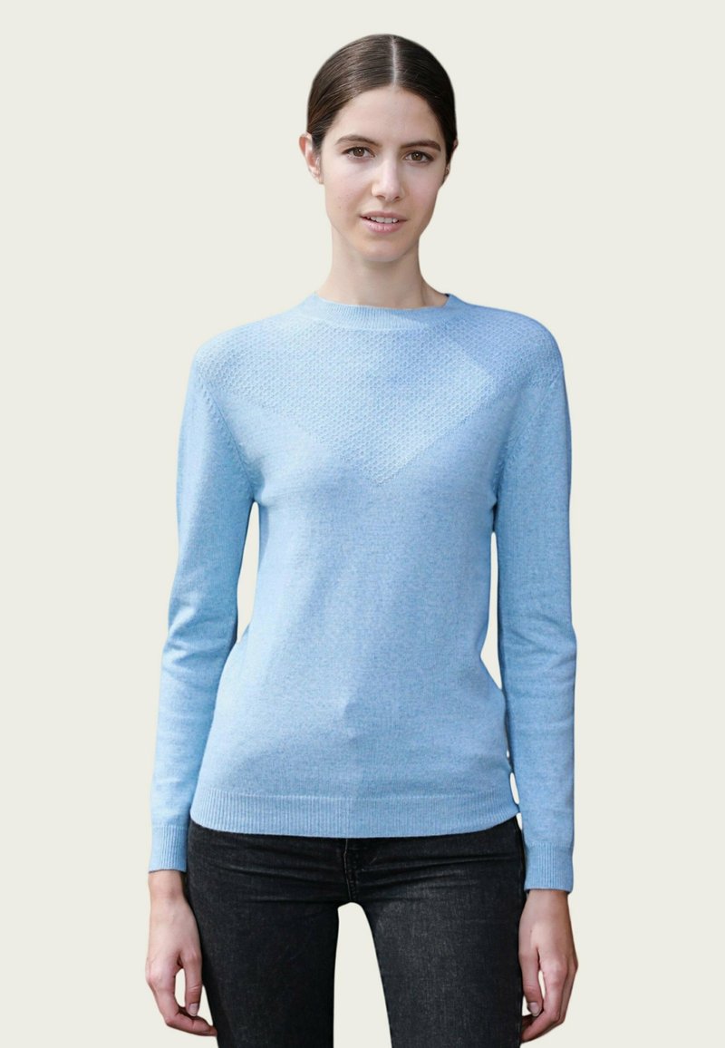 Pull en tricot bleu clair présentant un motif en losanges texturé sur la poitrine, avec des manches longues et un col rond. Associé à un jean noir.