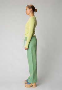 Top a maniche lunghe verde chiaro a righe abbinato a pantaloni a gamba larga verde chiaro, con cordoncino e scarpe con plateau in legno spesso.