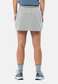 Grijze sportieve skort met een aangesloten tailleband, lichtgewicht materiaal en zakken. Gedragen met blauwe sportschoenen en grijze sokken.