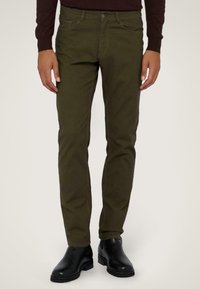 Pantalones ajustados de color verde oliva con una textura suave, que cuentan con bolsillos frontales, cierre de botón y están combinados con botas de cuero negras hasta el tobillo.